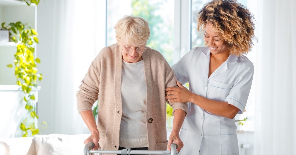 A woman helping an older person walk with a walker.