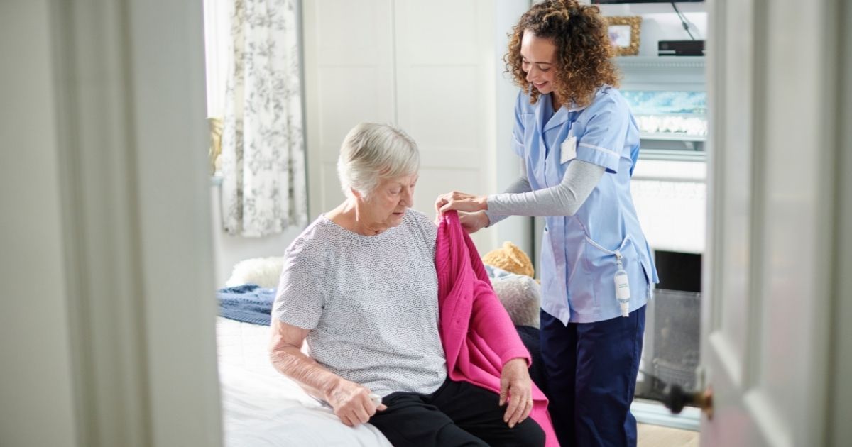 A nurse is helping an elderly woman with her dress.