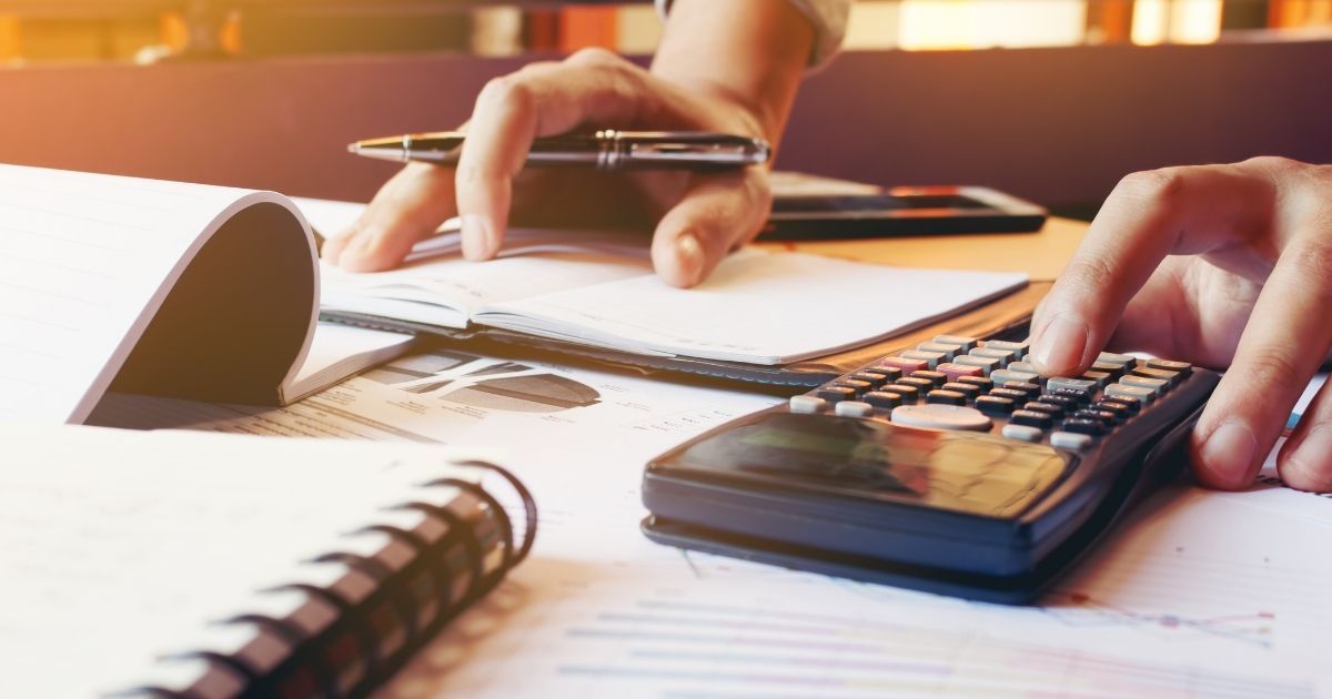 A person writing on paper with pens and calculator