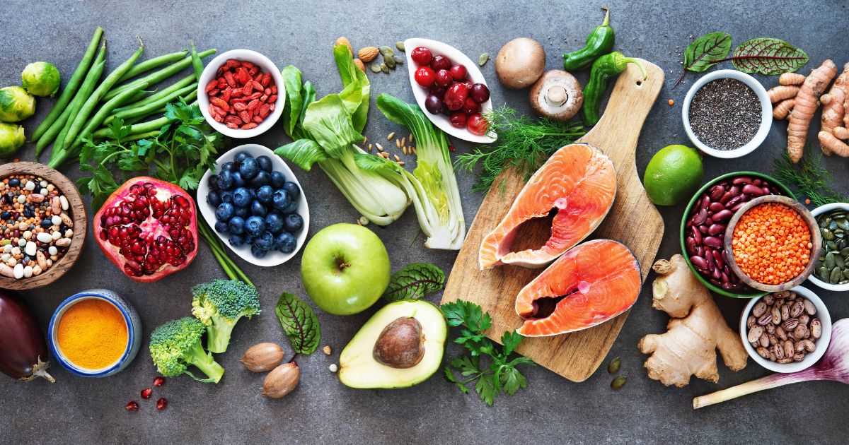 A table topped with fruits and vegetables next to an avocado.